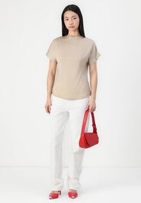 Haut beige à manches courtes, pantalon texturé blanc, sac à épaule rouge et escarpins rouges à bout pointu avec des accents argentés.