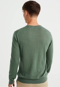 Grön, lätt långärmad tröja med rund hals; har ribbstickade muddar och fåll. Mjuk textur med en avslappnad passform.