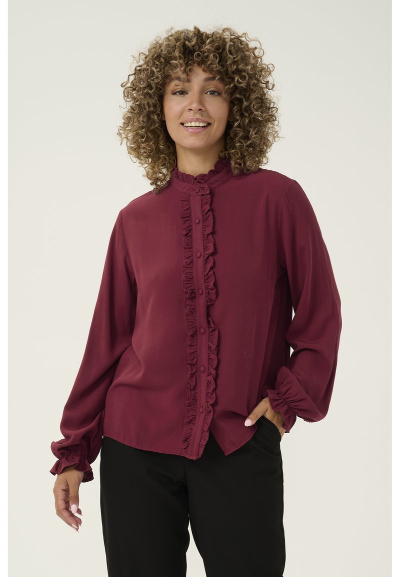 Burgundy blouse with ruffled front and cuffs, button closure, long sleeves, slim fit, and lightweight fabric against a neutral background.