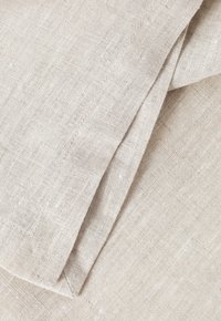 Linen fabric in light beige with a textured surface, featuring a clean edge seam and slight variations in thread for a natural look.