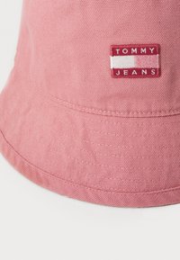 Chapéu de balde de algodão cor-de-rosa com um acabamento texturizado. Apresenta um patch de logo retangular em bordô com "TOMMY JEANS" em letras brancas.