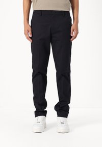 Mørkeblå bomullsbukser med slim fit, med knappelukking foran, beltehemper og sidelommer, kombinert med hvite joggesko.
