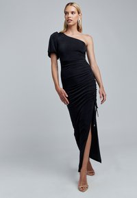 Schwarzes One-Shoulder-Kleid aus dehnbarem Stoff, mit Raffung an der Seite, hohem Schlitz und minimalistischem Design. Mit Kordeln akzentuiert.