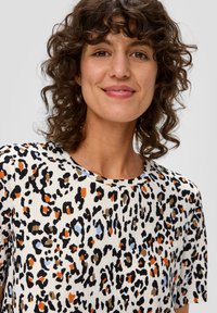 Halenka s leopardím vzorem s různobarevnými oranžovými, černými, modrými a béžovými skvrnami na světlem pozadí; krátké rukávy, kulatý výstřih, texturovaná tkanina.