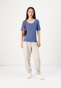 Modrý krátky rukáv s okrúhlym výstrihom, kombinovaný s voľnými svetlo béžovými nohavicami a bielymi teniskami. Jednoduchá hnedá crossbody taška.