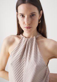Light pink halter top with vertical ribbed texture, featuring a gathered neckline and an open back design, made of a smooth fabric.
