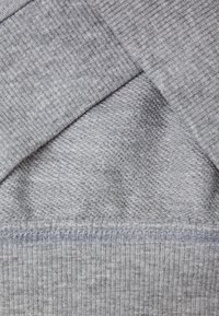 Strati di tessuto grigio con un motivo a maglia texturizzato e una finitura liscia, con cuciture visibili lungo i bordi e un dettaglio a coste nella parte inferiore.