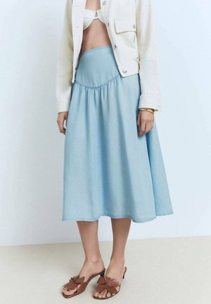 Light blue denim skirt with a gathered waistband, paired with a cream jacket. Brown sandals feature a floral design on the straps.