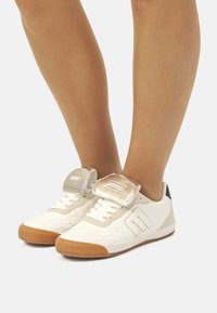 Weiße Sneaker mit einem strukturierten Design, grauen Akzenten, einem glänzenden silbernen Riemen und einer Sohle aus Gummi.