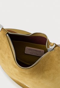 Borsa Coccinelle in camoscio giallo con cerniera argentata, interna in bordeaux e etichetta di autenticità in pelle beige.