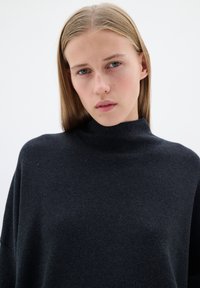 Mörkgrå, höghalset jumper i mjukt tyg med avslappnad passform. Har långa ärmar och en minimalistisk design, inga synliga mönster eller detaljer.