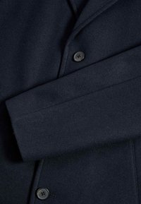 Donker marineblauw wollen jas met een pieklapel, enkele knoopsluiting en een gladde textuur met een getailleerde pasvorm.