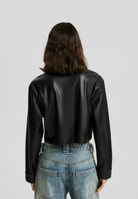 Skórzana kurtka z czarnego materiału o gładkiej fakturze i długich rękawach, zestawiona z niebieskimi dżinsami z wysokim stanem z kieszeniami na łaty.