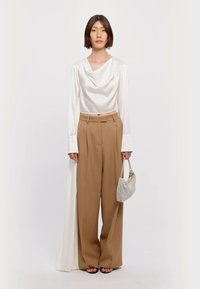 Σατινέ λευκή μπλούζα με ντραπέ λαιμόκοψη, καφέ παντελόνι με ψηλή μέση και φαρδιά πόδια, και μία μικρή τσάντα από ασημένια χάντρα. Απλά μαύρα σανδάλια.