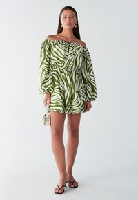 Roheline-valge triibuline õlgadest paljastav kleit, millel on õhupalli varrukad, piht sisse võetud, lehvikseelik; kombineeritud mustade varbavaheplätude ja väikese kotiga.