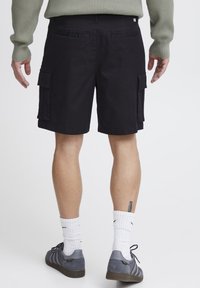 Schwarze Cargo-Shorts mit geradem Schnitt, seitlichen Taschen und glatter Textur. Getragen mit grauen Sneakers und weißen Socken.