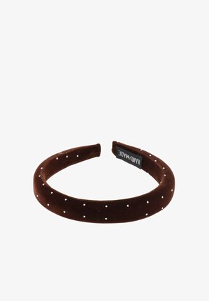 Diadema de terciopelo marrón con pequeños lunares blancos, forma redondeada y una etiqueta de la marca en el interior.