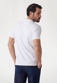 White short-sleeve t-shirt made of soft fabric, featuring a round neck and a smooth texture, paired with blue denim pants.
