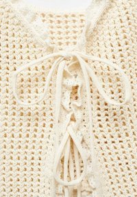 Pullover lavorato a maglia color crema con tessitura aperta, dotato di scollatura a laccetti con nastri e dettagli a scallop lungo il collo.
