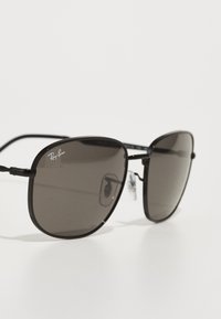 Ochelari de soare de tip black metal cu lentile mari și întunecate. Caracteristicile includ un cadru subțire și suporturi pentru nas, prezentând logo-ul Ray-Ban pe lentila stângă.