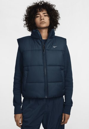 Gilet imbottito blu navy con collo alto, zip frontale e logo Nike sul lato sinistro del petto. Caratterizzato da sezioni trapuntate e due tasche laterali.