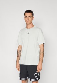Lys grå kortærmet t-shirt med et sort Jordan-logo på brystet, parret med sorte mesh shorts med hvid kant og detaljer.