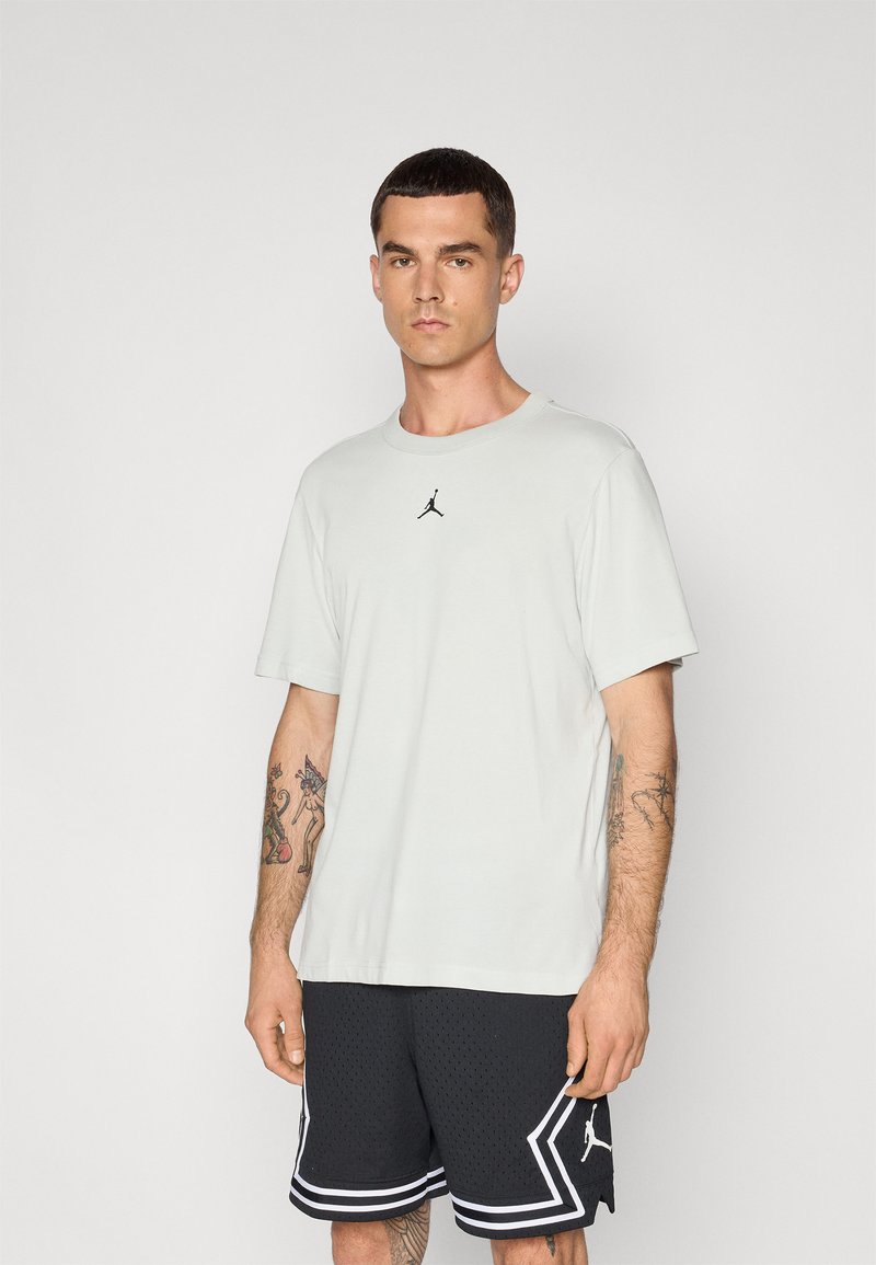 Lys grå t-skjorte med korte ermer og svart Jordan-logo på brystet, kombinert med svarte mesh-shorts med hvite kanter og detaljer.