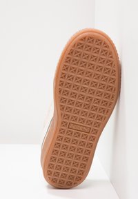 Semelle de sneaker Puma en caoutchouc gomme texturé avec un motif pyramidal. Tige beige avec des accents minimalistes, mettant en avant un design simple.