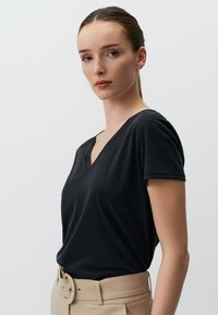 Czarna koszulka V-neck z krótkimi rękawami, gładka tekstura, zestawiona z beżowymi spodniami o wysokim stanie z szerokim paskiem i klamrą.