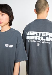 Gray oversized t-shirt with short sleeves. Front features "VERTERE BERLIN" in white text. Back displays large white text and a logo detail.