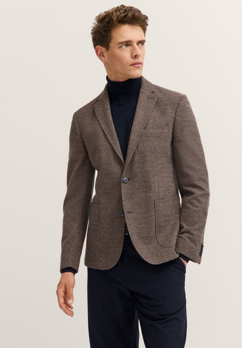 Braune Hahnentritt-Blazer mit Reverskragen, zwei Knöpfen und seitlichen Taschen, kombiniert mit einem schwarzen Rollkragenpullover. Strukturierter Wollmischstoff.