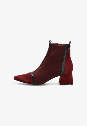 Botines de ante rojo con punta puntiaguda, con detalles negros texturizados y un tacón bloque grueso. Paneles laterales elásticos para facilitar su uso.