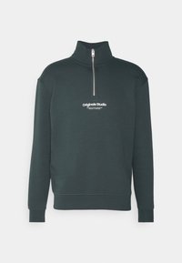 Sötétzöld, cipzáras pulóver magas gallérral. Bordás mandzsettákkal és derékrésszel rendelkezik. Az elején az 'Originals Studio' logó látható.