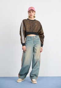 Cropped black leopard print sweatshirt with white stripes on sleeves, paired with loose light blue jeans featuring orange side stripes and beige sneakers.