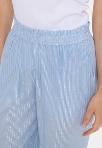 Light blue, pleated pants with a shiny, textured finish and an elastic waistband. Vertical stripes create a subtle pattern.