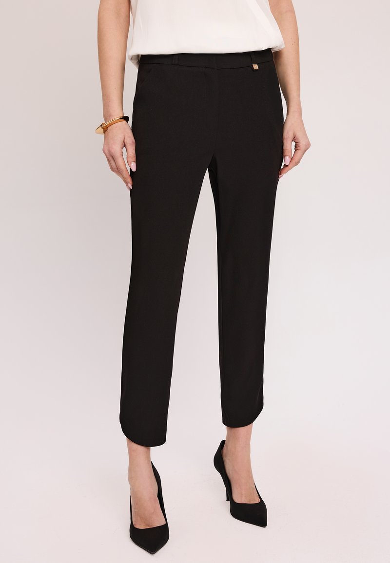 Czarne dopasowane spodnie o gładkiej teksturze, długości do kostek, z delikatnym plisowaniem z przodu. Posiadają mały złoty akcent w talii.