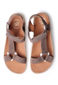 Bruna mockasklippor med korsade remmar, beige sula och vita detaljer i metall. Platt sula med sömnadsdetaljer.