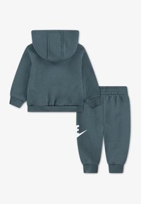 Σετ αθλητικών ρούχων δύο τεμαχίων. Φούτερ με κουκούλα και παντελόνι φόρμας σε σκούρο τιρκουάζ, με ριμπ μανσέτες και μεγάλο λευκό λογότυπο Nike στο παντελόνι.