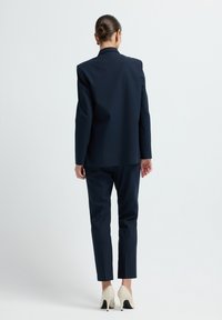 Námornická obleková souprava s strukturovaným sáčkem a slim-fit kalhotami. Hladká textura, jemný proužkovaný vzor, doplněná krémovými lodičkami na podpatku.