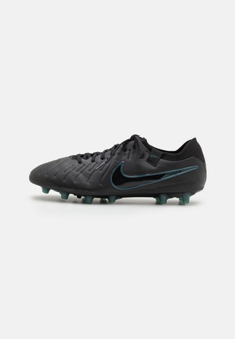 Botas de fútbol negras con parte superior de cuero texturizado, con un logo de Nike en azul verdoso y cinco tacos moldeados en una suela oscura para tracción.