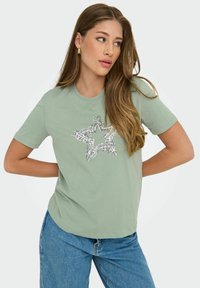 Lys grøn bomulds t-shirt med et sølvfarvet pailletstjernedesign på forsiden, med korte ærmer og en afslappet pasform.