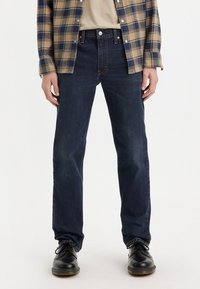 Dark blue denim jeans with a straight-leg cut, paired with a plaid flannel shirt. Shoes are black leather with a rounded toe.