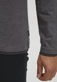 T-shirt grigio a maniche lunghe con scollatura rotonda, caratterizzato da un'etichetta laterale e un colletto a contrasto. Tessuto morbido con una texture liscia.