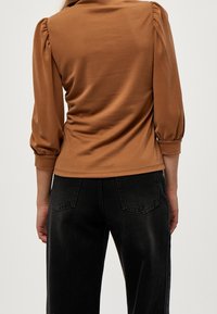 Brun figursydd topp med puffärmar, tillverkad av mjukt tyg. Kombinerad med högmidjade svarta jeans med en klassisk fickdesign.