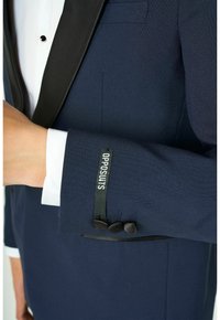 Marineblaues Sakko mit einem schwarzen Satinrevers, drei schwarzen Knöpfen an den Manschetten und einem Etikett mit der Aufschrift "OPPOSUITS" auf dem Ärmel.