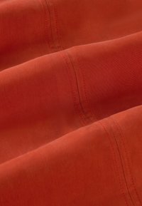 Tissu orange rouille avec double couture visible et plis doux, mettant en valeur la texture et les coutures.