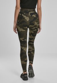 Högmidjade camouflagemönstrade leggings i grön och svart med en slät textur, figurnära design och stretchigt material. Bärs med mörka träningsskor.