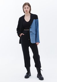 Blazer a dos tonos en negro y mezclilla con dos botones, combinado con pantalones negros con cordón y botas negras con cordones. Textura suave en toda la prenda.