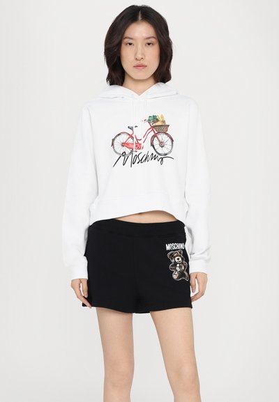 White cropped hoodie featuring a red bicycle graphic with a basket; paired with black shorts displaying a bear logo in embroidery.