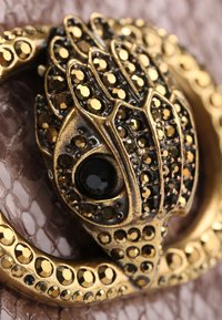 Złoty dekoracyjny zapięcie z misternymi wzorami z czarnych i złotych cyrkonii, z wyraźnym czarnym kamieniem ozdobnym.